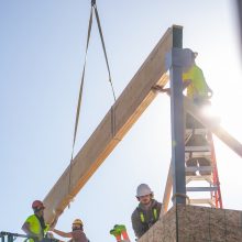 construction workers on a roof placing a board hanging from a crane