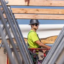 A construction worker with a grey helmet, cool sunglasses and a neon green shirt framing a building